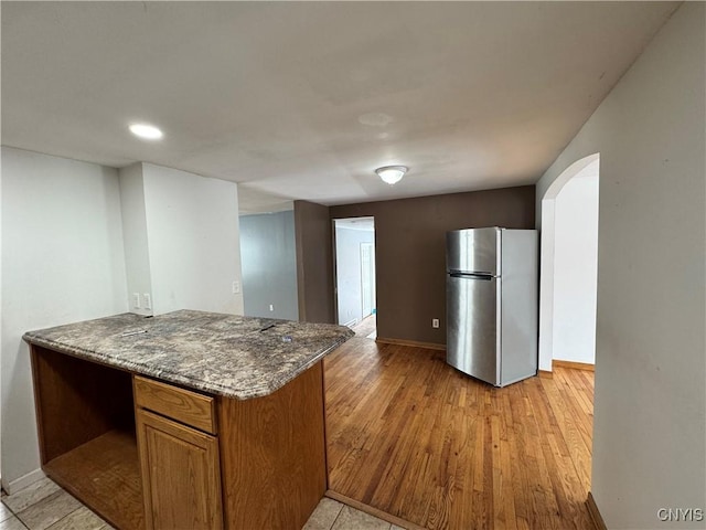 kitchen featuring arched walkways, brown cabinets, freestanding refrigerator, a peninsula, and light wood-style floors