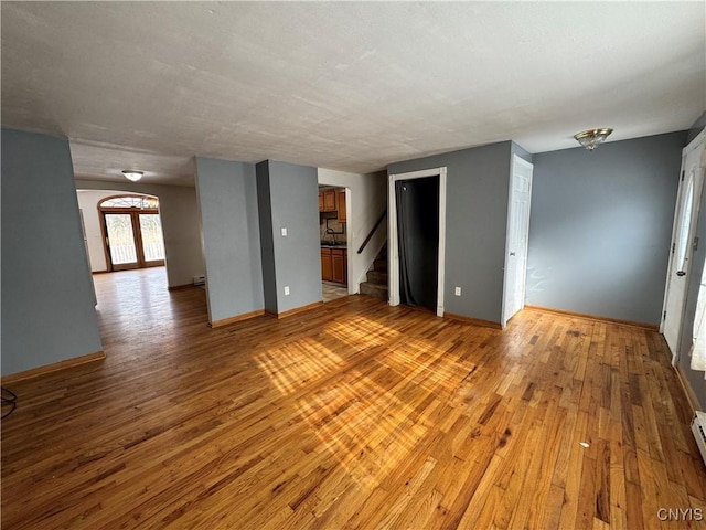 empty room featuring a baseboard heating unit, light wood-style flooring, stairs, and baseboards