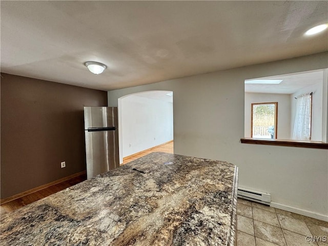 kitchen featuring a baseboard heating unit, freestanding refrigerator, arched walkways, and baseboards