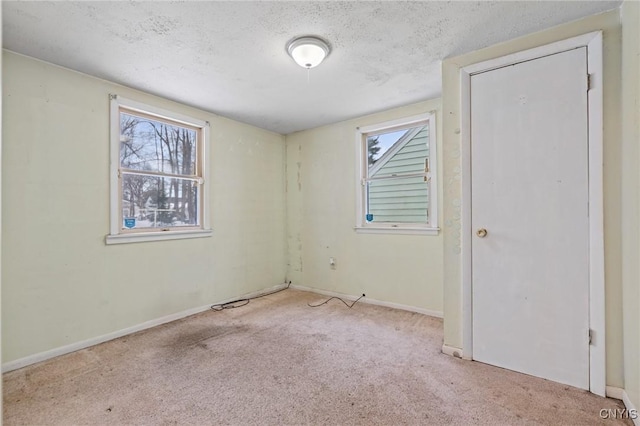 unfurnished room featuring light colored carpet, a textured ceiling, and baseboards