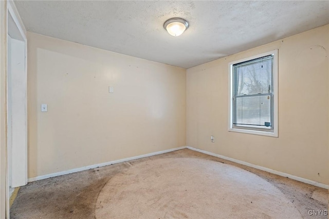 spare room featuring baseboards, a textured ceiling, and light colored carpet