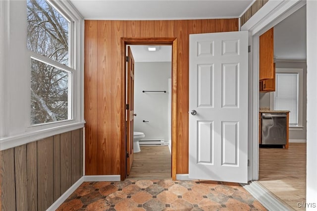 hallway featuring a baseboard heating unit, plenty of natural light, and wooden walls