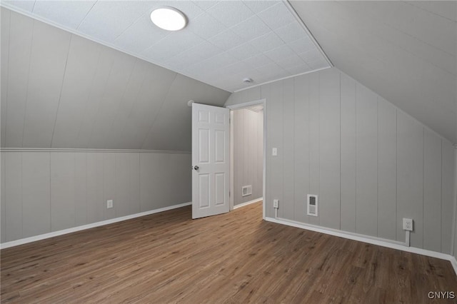 additional living space with lofted ceiling, wood finished floors, visible vents, and baseboards