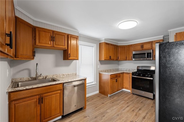 kitchen with crown molding, light wood finished floors, stainless steel appliances, brown cabinetry, and a sink