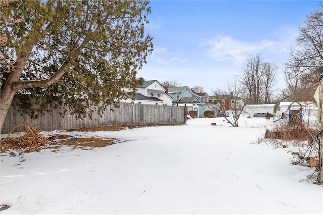 yard covered in snow with a residential view and fence