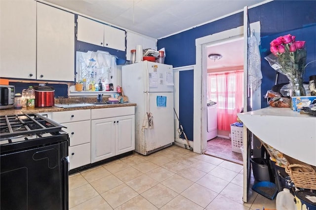 kitchen with freestanding refrigerator, washer / clothes dryer, white cabinets, and gas range