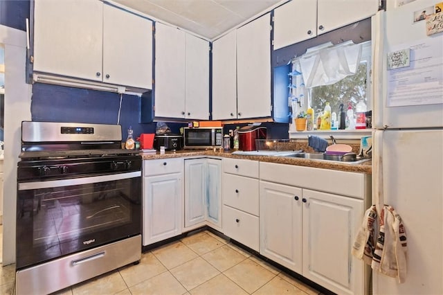 kitchen featuring light tile patterned floors, white cabinets, dark countertops, appliances with stainless steel finishes, and a sink