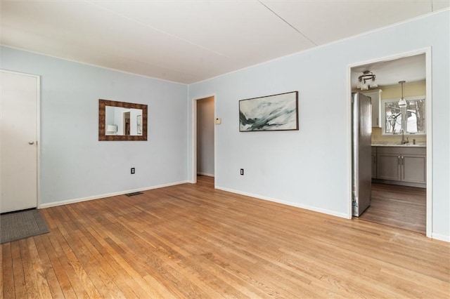 empty room with baseboards, a sink, visible vents, and light wood-style floors