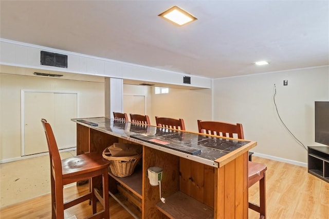 bar with light wood finished floors, baseboards, visible vents, and ornamental molding