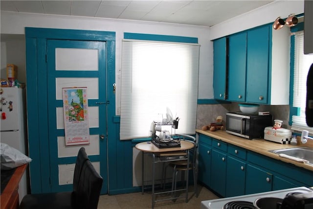 kitchen featuring blue cabinetry, light countertops, freestanding refrigerator, a sink, and range