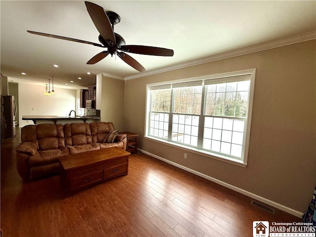 living area featuring visible vents, baseboards, dark wood-style floors, and crown molding