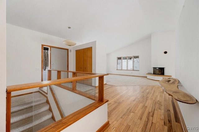 bonus room featuring stairway, light wood-type flooring, a glass covered fireplace, and lofted ceiling