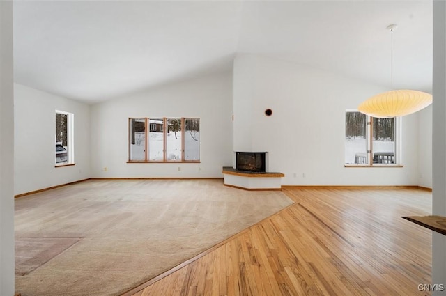 unfurnished living room featuring high vaulted ceiling, baseboards, a multi sided fireplace, and light wood finished floors