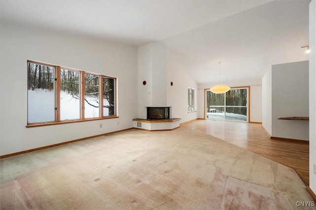 unfurnished living room with high vaulted ceiling, baseboards, light colored carpet, and a multi sided fireplace