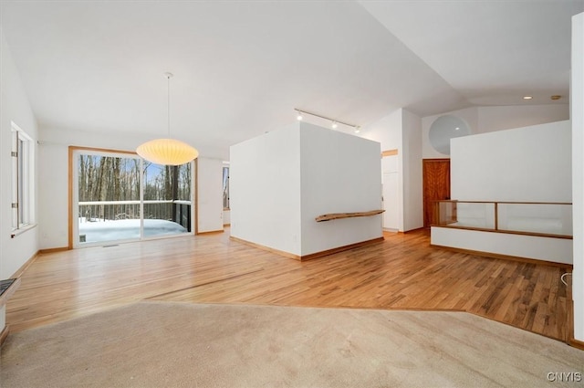 empty room with vaulted ceiling, track lighting, light carpet, and light wood-style floors