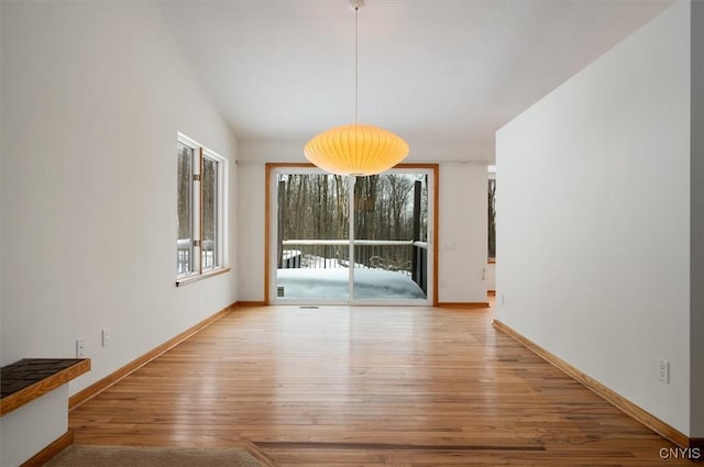 unfurnished dining area with baseboards, vaulted ceiling, and light wood-style floors