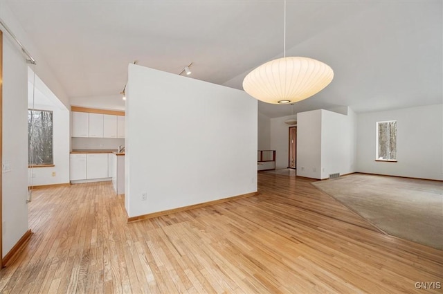 unfurnished living room with visible vents, light wood-style flooring, vaulted ceiling, track lighting, and baseboards