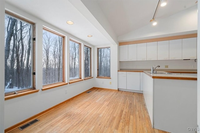 kitchen featuring a sink, visible vents, white cabinets, vaulted ceiling, and light countertops