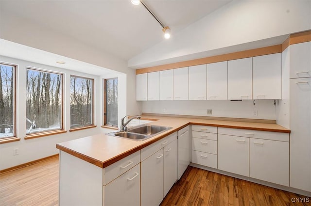 kitchen with a peninsula, a sink, white cabinets, vaulted ceiling, and light countertops