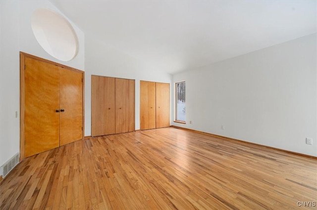 unfurnished bedroom with light wood-type flooring, visible vents, and multiple closets