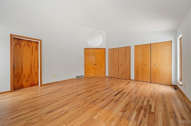 unfurnished bedroom featuring multiple closets, visible vents, high vaulted ceiling, and light wood finished floors