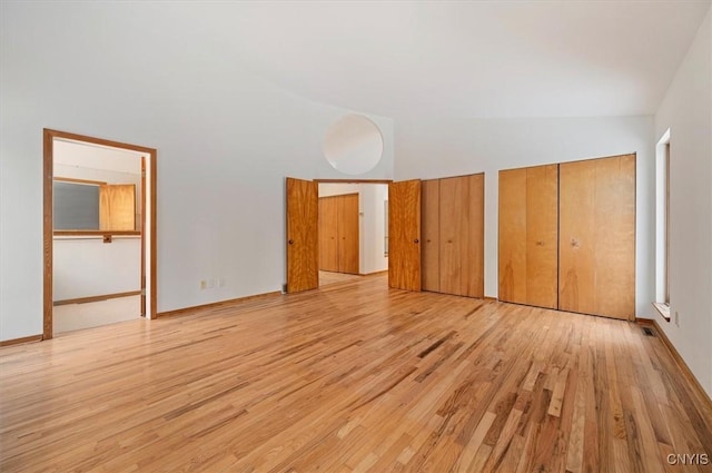 unfurnished bedroom with a towering ceiling, light wood finished floors, visible vents, and multiple closets