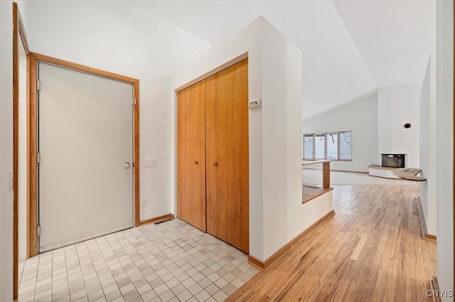 corridor with light wood-type flooring, vaulted ceiling, and baseboards