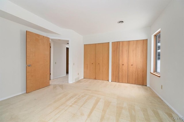 unfurnished bedroom featuring multiple closets, light carpet, visible vents, and baseboards