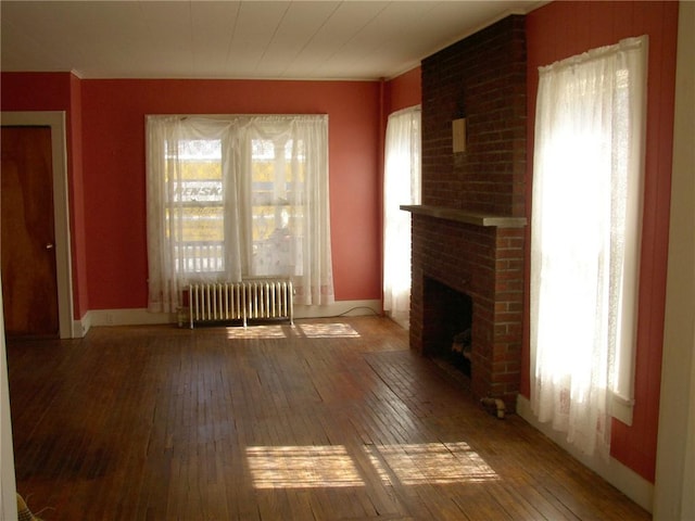 unfurnished living room with hardwood / wood-style floors, radiator heating unit, a brick fireplace, and baseboards