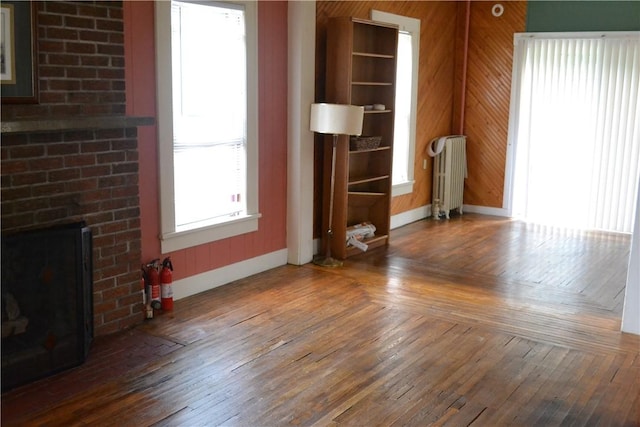 unfurnished living room with hardwood / wood-style floors, radiator heating unit, a fireplace, and baseboards