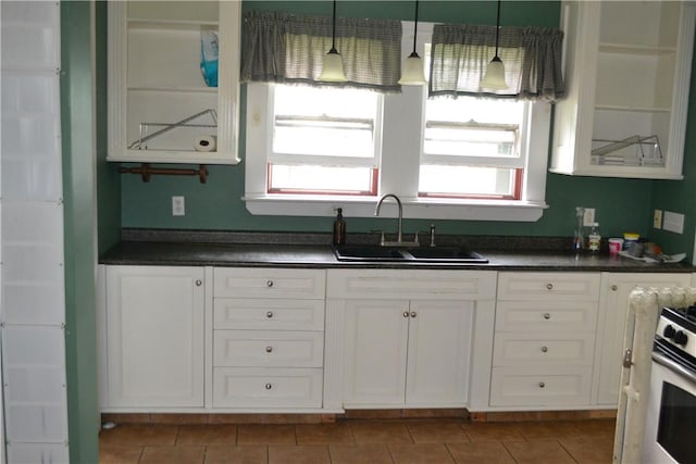 kitchen featuring dark countertops, hanging light fixtures, white cabinets, a sink, and gas range