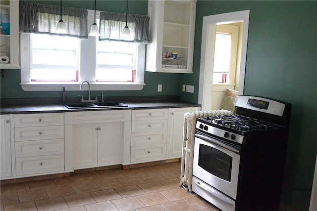 kitchen featuring dark countertops, glass insert cabinets, gas stove, white cabinetry, and a sink