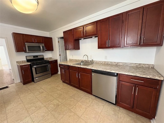 kitchen with reddish brown cabinets, stainless steel appliances, light countertops, visible vents, and a sink