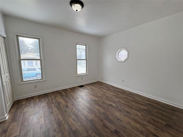 spare room featuring dark wood-style flooring, visible vents, and baseboards