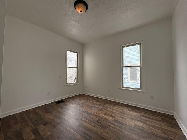 unfurnished room with dark wood-style flooring, visible vents, a textured ceiling, and baseboards