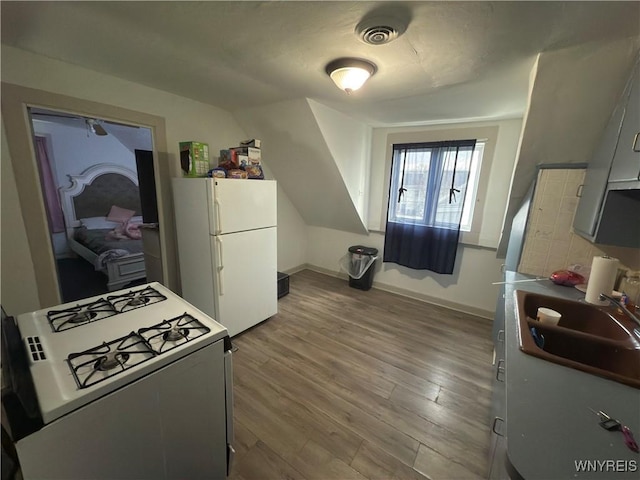 kitchen featuring visible vents, a sink, wood finished floors, white appliances, and baseboards