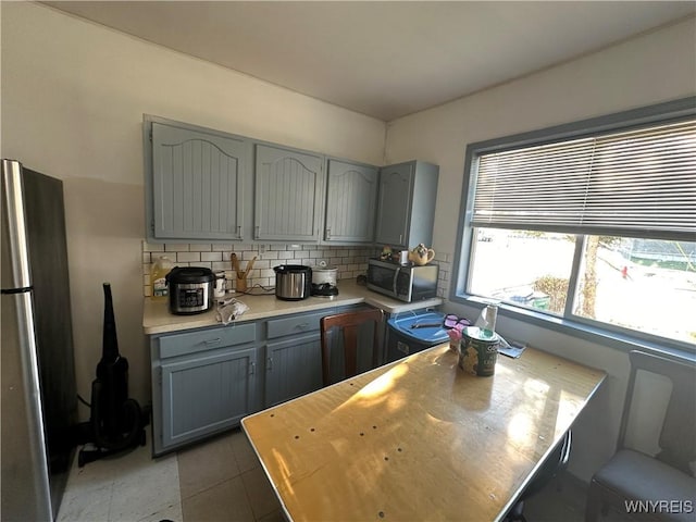 kitchen featuring tasteful backsplash, light countertops, gray cabinetry, appliances with stainless steel finishes, and tile patterned flooring