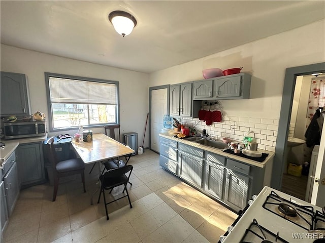 kitchen with tasteful backsplash, stainless steel microwave, gray cabinets, light countertops, and a sink