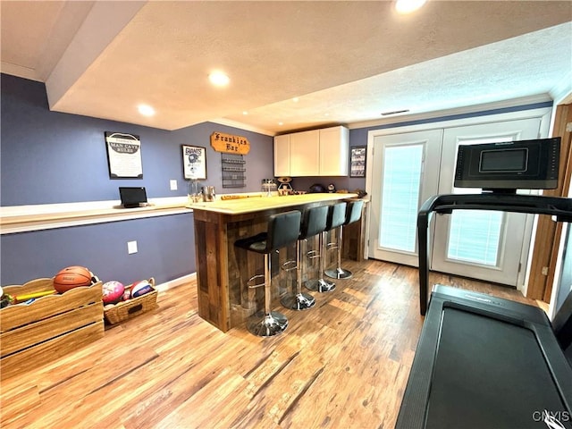 interior space featuring light wood-style flooring, wet bar, a textured ceiling, crown molding, and recessed lighting