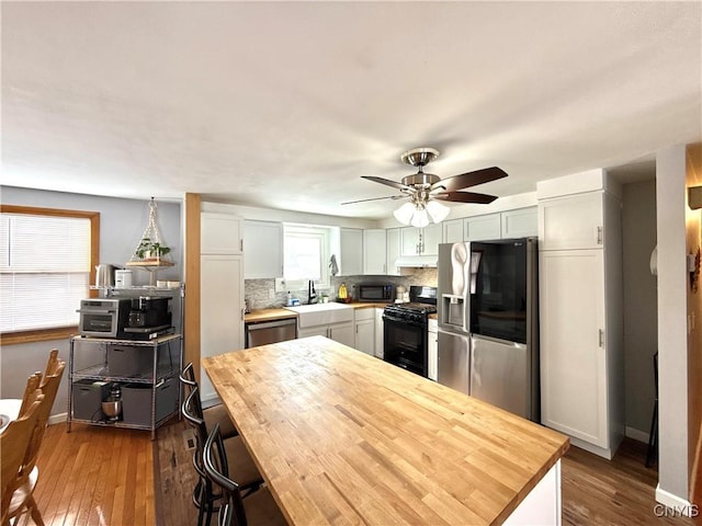 kitchen with a sink, black appliances, tasteful backsplash, and wood finished floors