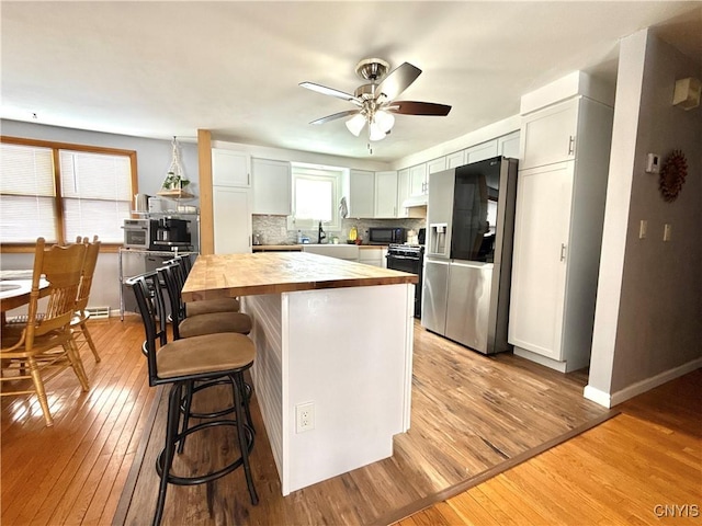 kitchen featuring white cabinetry, wooden counters, light wood-type flooring, black appliances, and tasteful backsplash