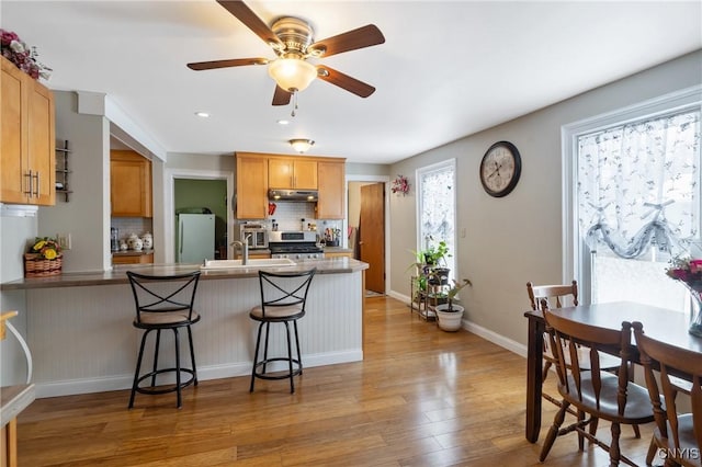 kitchen with a breakfast bar area, freestanding refrigerator, gas stove, a peninsula, and under cabinet range hood