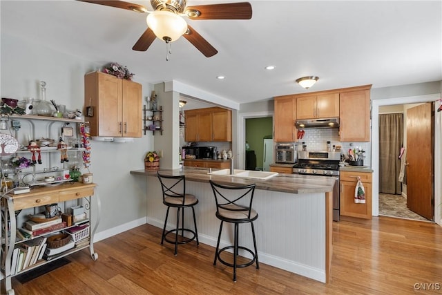 kitchen featuring a peninsula, a breakfast bar area, gas stove, and under cabinet range hood