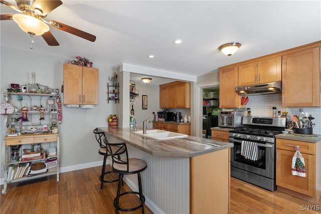 kitchen with under cabinet range hood, a peninsula, a sink, gas stove, and a kitchen bar