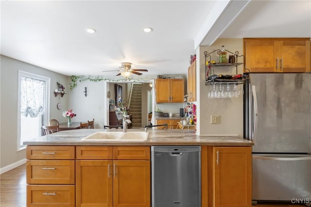 kitchen featuring stainless steel appliances, a sink, light wood-style floors, light countertops, and brown cabinets