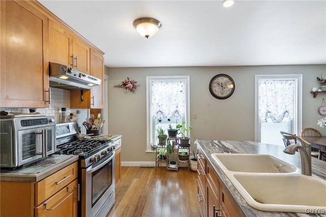 kitchen with tasteful backsplash, a healthy amount of sunlight, under cabinet range hood, a sink, and gas stove