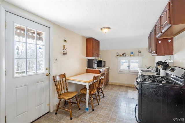 kitchen featuring stainless steel gas range, brown cabinets, light countertops, and baseboards