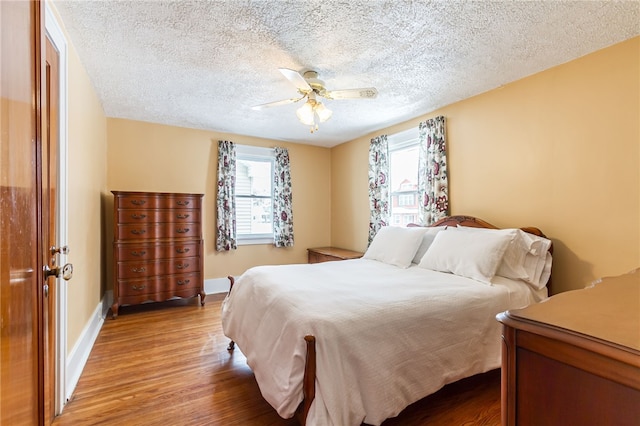 bedroom featuring light wood finished floors, multiple windows, a ceiling fan, and baseboards