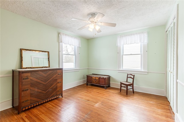 sitting room with a textured ceiling, light wood-type flooring, a ceiling fan, and baseboards