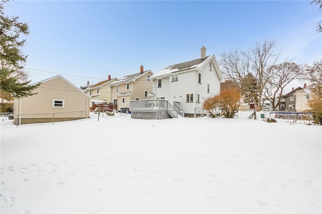 snow covered back of property featuring a residential view, fence, and a wooden deck